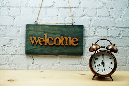 Wooden Welcome sign and alarm clock with space copy on white brick wall backgroundの写真素材
