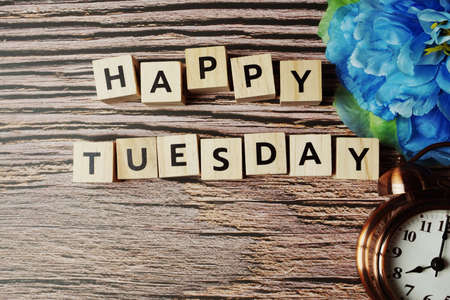 Happy Tuesday alphabet letter with alarm clock and blue flower on wooden background.の写真素材