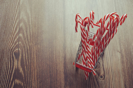 Christmas Candy Cane in mini shopping cart on wooden background