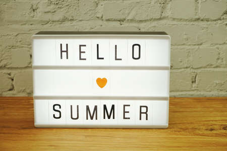 Hello Summer word in light box on white brick wall and wooden backgroundの写真素材