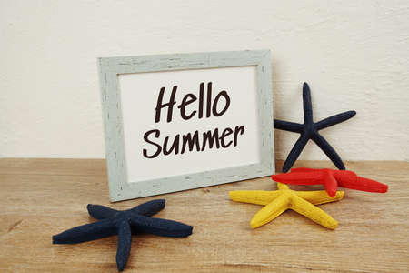 Hello Summer typography text with starfish decoration on wooden and white wall backgroundの写真素材