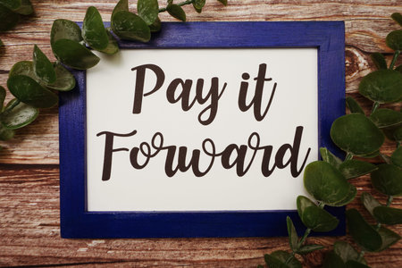Pay it Forward written on blue frame with green leave flat lay on wooden background