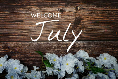 Welcome July text and blue flower decoration on wooden backgroundの写真素材