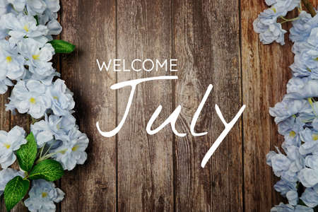 Welcome July text and blue flower decoration on wooden backgroundの写真素材