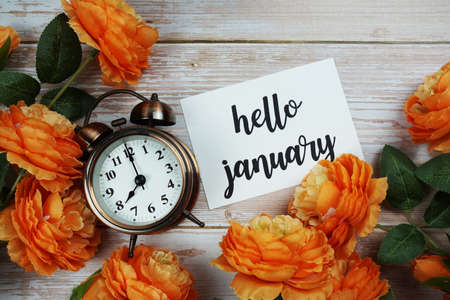 Hello January card and alarm clock with orange flower decoration on wooden backgroundの写真素材