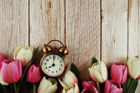 Vintage alarm clock with pink tulip flower bouquet on wooden backgroundの写真素材