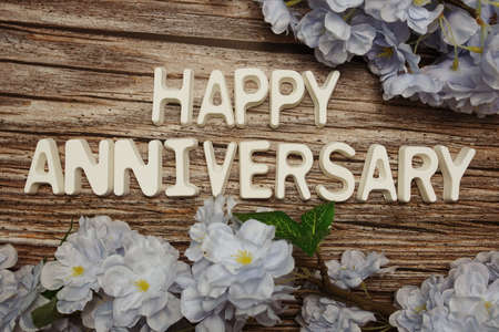 Happy Anniversary alphabet letter with flower decoration on wooden backgroundの写真素材