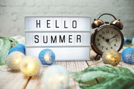 Hello Summer word in lightbox with alarm clock and Monstera Leave decoration on wooden backgroundの写真素材