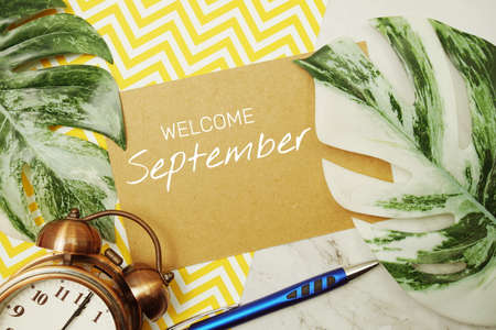 Welcome September typography text on paper card with alarm clock and Monstera leaveの写真素材
