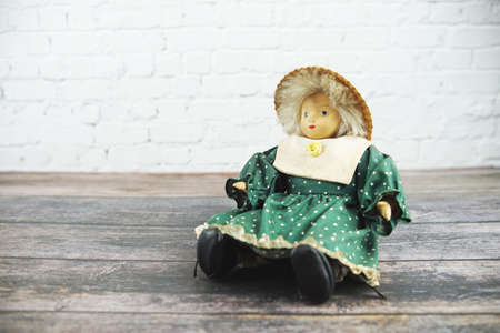 Vintage doll wearing with green dress sit on wooden floor over on white brick wall backgroundの写真素材
