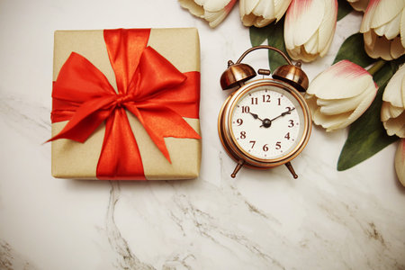 Gift boxes with alarm clock and tulip flower bouquet on marble background
