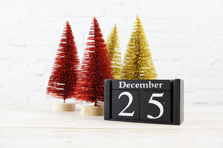 December 25th on the wooden calendar with little christmas tree on white brick wall background