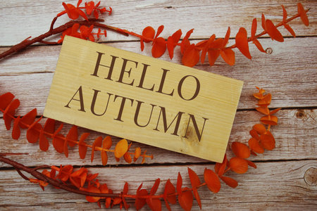 Hello Autumn text on wooden board with orange leaves decorate on wooden background