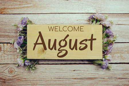 Welcome August text on wooden board with flowers frame on wooden backgroundの写真素材