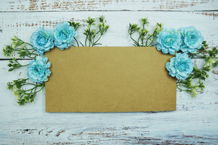 Frame of flowers with paper card for text on wooden background