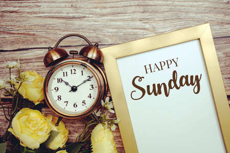 Happy Sunday typography text with alarm clock and flower decoration on wooden backgroundの写真素材