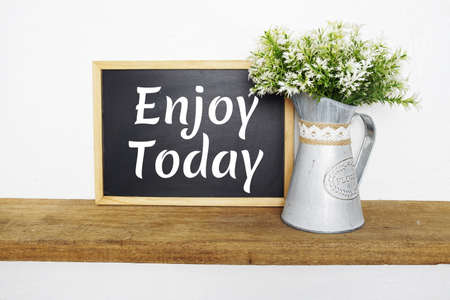 Blackboard with the text ENJOY TODAY decorate with artificial plant in watering plant on wooden shelvesの写真素材