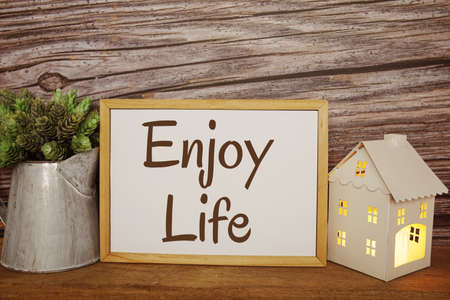 Blackboard with the text ENJOY LIFE decorate with artificial plant in watering plant and LED candle in house lantern on wooden backgroundの写真素材