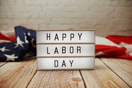 Happy Labor Day word in lightbox and American flag on wooden background