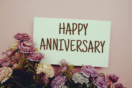 Happy Anniversary typography text with flowers on pink backgroundの写真素材