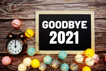 Goodbye 2021 text on wooden blackboard with alarm clock and LED cotton balls decoration on wooden backgroundの写真素材