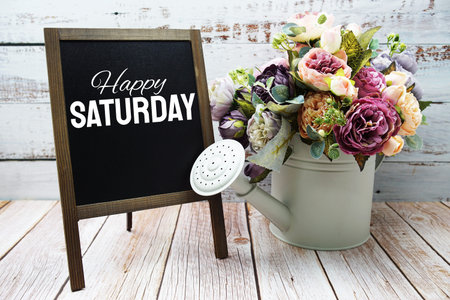 Happy Saturday text on blackboard easel with flower bouquet on wooden backgroundの写真素材