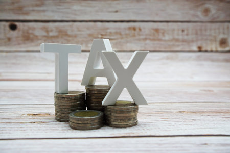 TAX alphabet letters with coin stack on wooden background