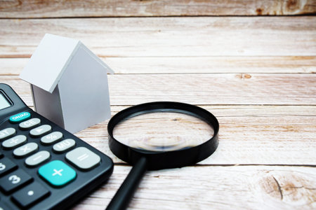 White Model House with magnifying glass and calculator on wooden background, realestate concept