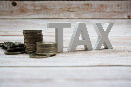 TAX alphabet letters with coin stack on wooden background