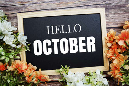 Hello October typography text written on wooden blackboard with flower bouquet decorate on wooden backgroundの写真素材