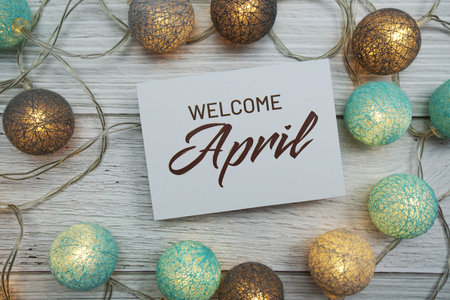 Welcome April text on paper card with LED cotton balls top view on wooden background