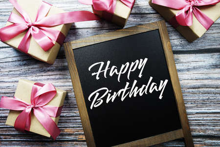 Happy Birthday text on blackboard with gift boxes on wooden backgroundの写真素材