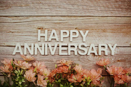 Happy Anniversary alphabet letters with flowers frame on wooden backgroundの写真素材