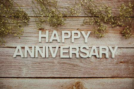 Happy Anniversary alphabet letters with flowers frame on wooden backgroundの写真素材