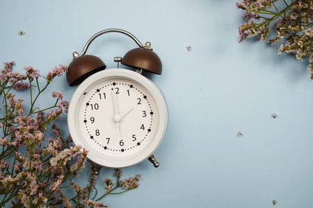 Alarm clock and flowers with space copy on blue background