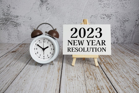 2023 New Year Resolution text message and alarm clock on wooden background