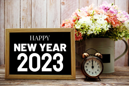 Happy New Year 2023 typography text on blackboard with alarm clock and flower in watering vaseの写真素材