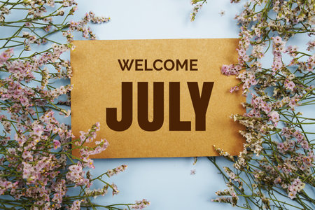 Welcome July written on paper card with flower frame decoraton on pink backgroundの写真素材