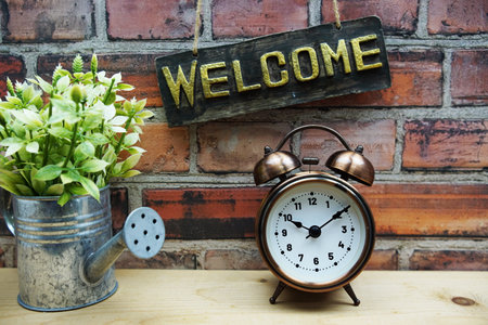 Welcome sign hanging with alarm clock on old brick wall backgroundの写真素材