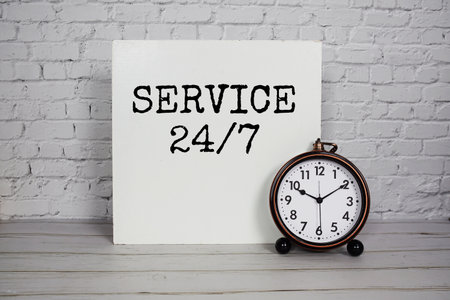 24/7 Service alphabet letters and alarm clock on white brick wall backgroundの写真素材
