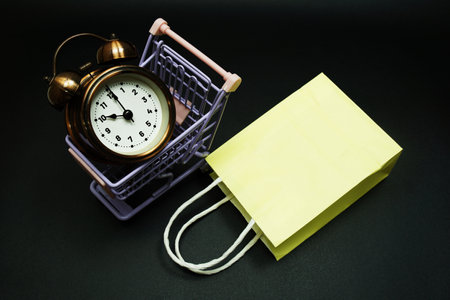 Trolley cart and shopping bag with alram clock with space copy on black backgroundの写真素材