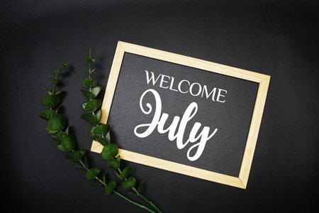 Welcome July text message on wooden blackboard with green leaf decorationの写真素材