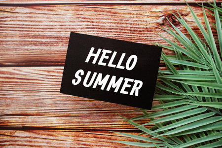 Hello Summer text message top view on wooden background with green leaf decorationの写真素材