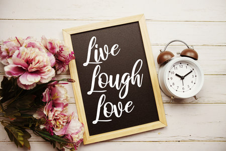 Live Lough Love text message with alarm clcok and flower decoration on wooden backgroundの写真素材