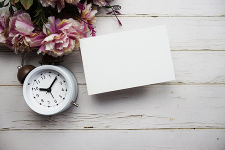 Empty card mockup with flower bouquet and alarm clock on wooden backgroundの写真素材