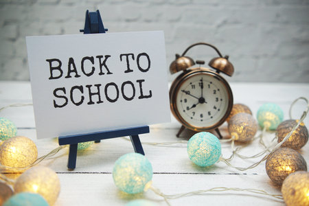 Back to School text and alarm clock on white brick wall and wooden background