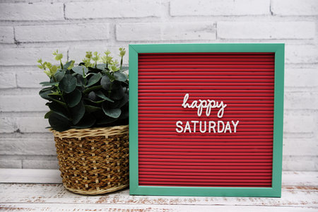 Happy Saturday text on Letter Board artficial plant decoration on wooden background