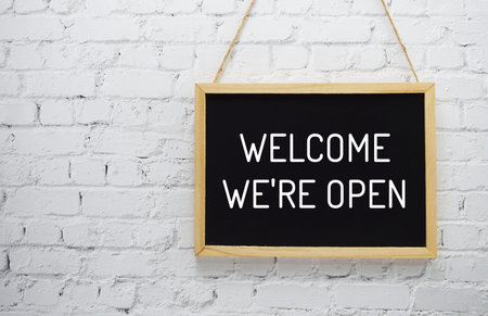 Welcome We are Open typography text on blackboard hanging against on the wall background