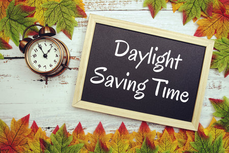 Daylight Saving Time typography text on wooden blackboard with alarm clock and maple leavesの写真素材