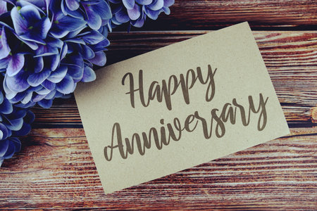 Happy Anniversary typography text on paper card decorate with flower on wooden background